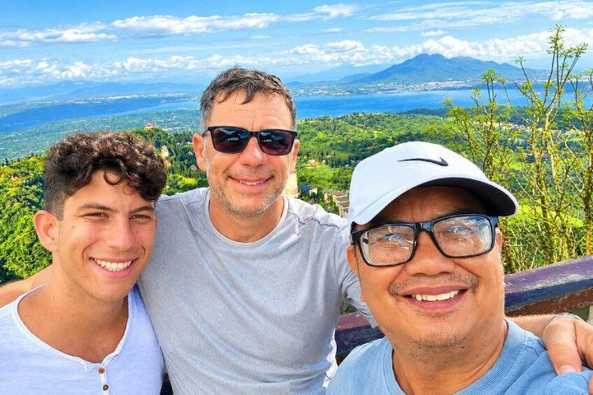 Three people standing on a high vantage point overlooking a mountainous landscape with a body of water in the distance. 2