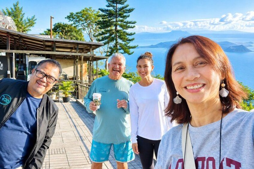 A group of people on a wooden deck overlooking a scenic landscape with mountains and a body of water. 3
