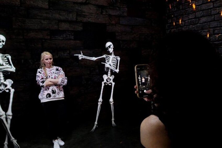 A person in a patterned shirt and a skeleton figure in a dark setting. 4