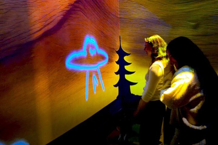 A neon sign of a UFO, a person in a white shirt, and another person in a dark jacket. 2