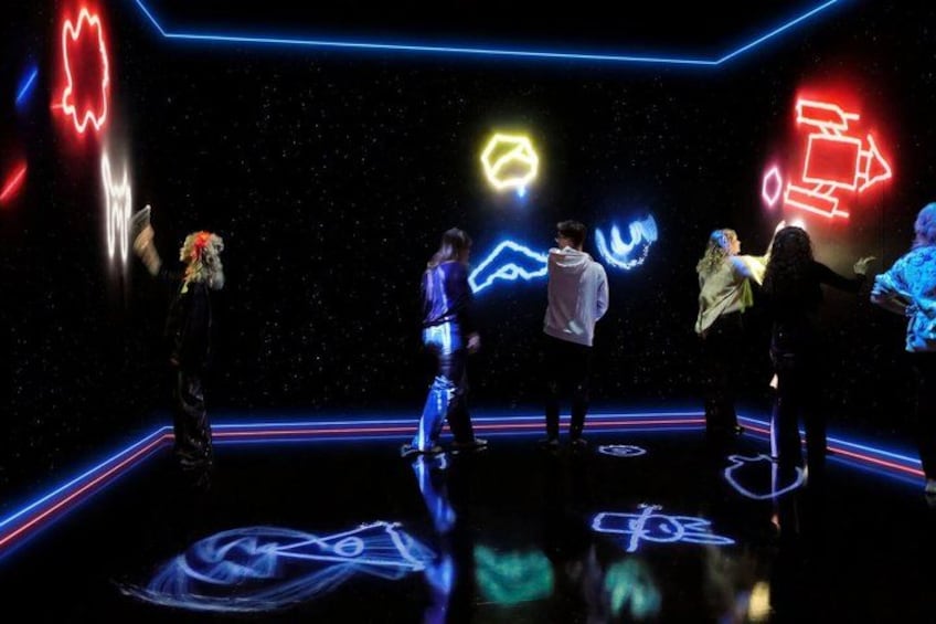 A group of people in a dark room with neon light outlines and symbols on the floor. 5
