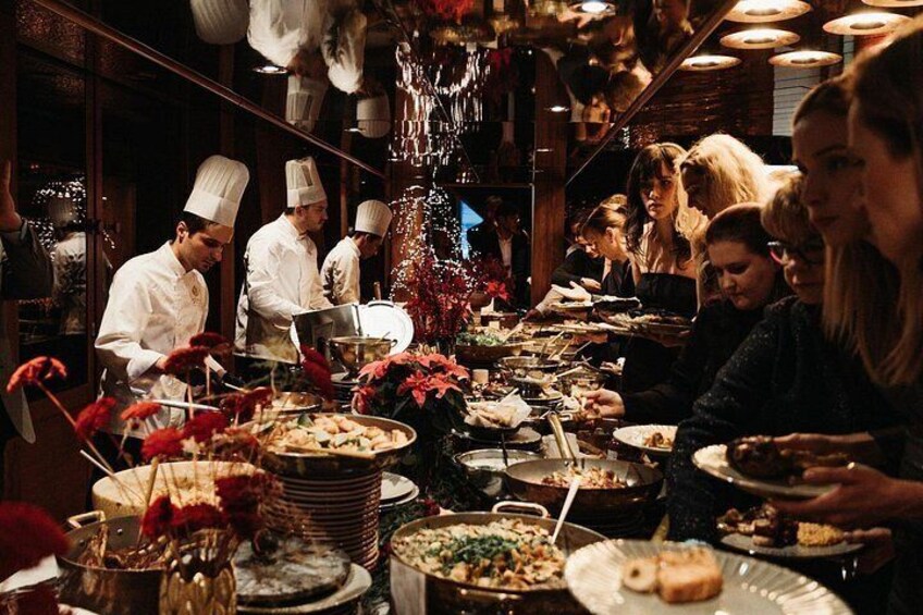 A buffet with various dishes, chefs serving, and guests eating. 3