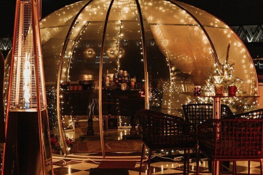 A glass-domed structure with string lights, a tall building, and outdoor seating. 3