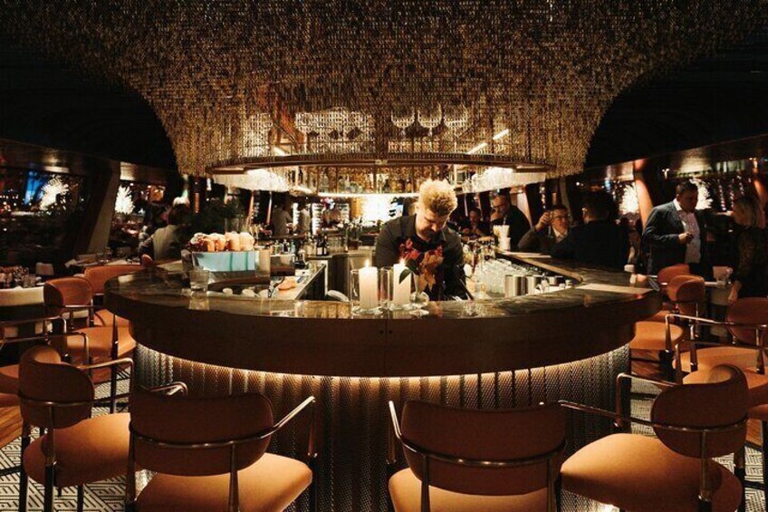 A bar with a bartender preparing drinks. There are several patrons seated at tables. 2
