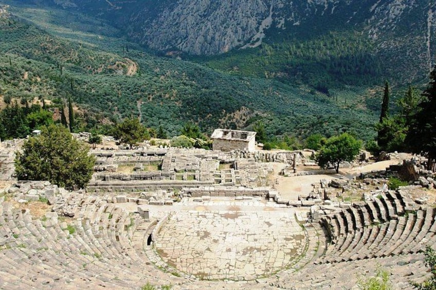 An ancient amphitheater with stone seating and a central stage, surrounded by rugged mountains and sparse vegetation. 4