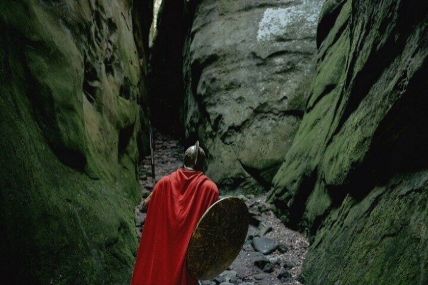 A person in a red cloak walking through a narrow canyon with rocky walls. 2