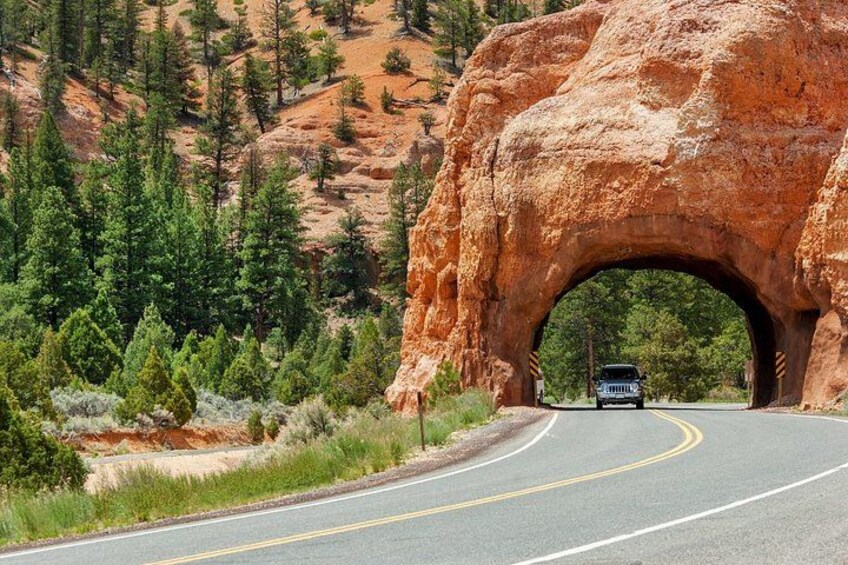 A road passing through a natural rock arch formation with a vehicle approaching. 5