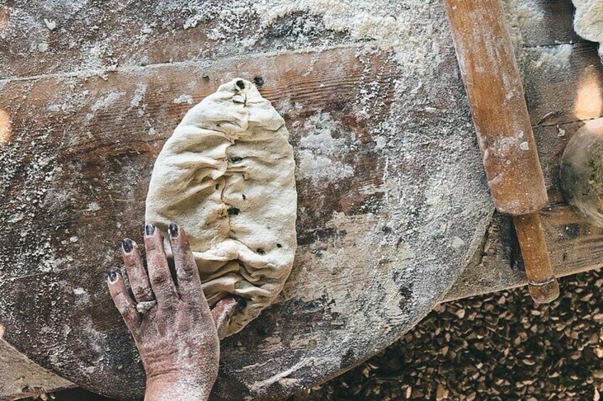 A hand holding a piece of dough on a wooden surface with a rolling pin nearby. 1