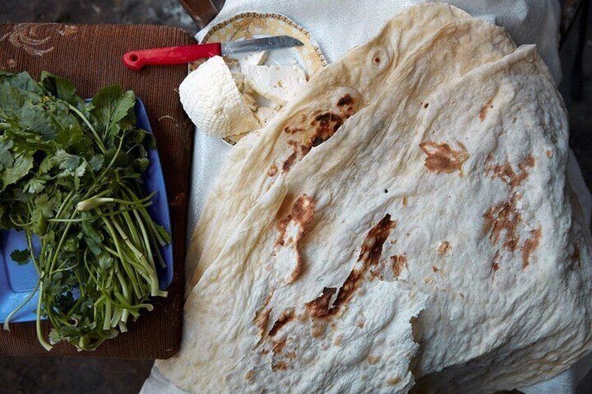 A large piece of flatbread with some brown spots, a red-handled knife, and a blue plate with green leafy vegetables. 4