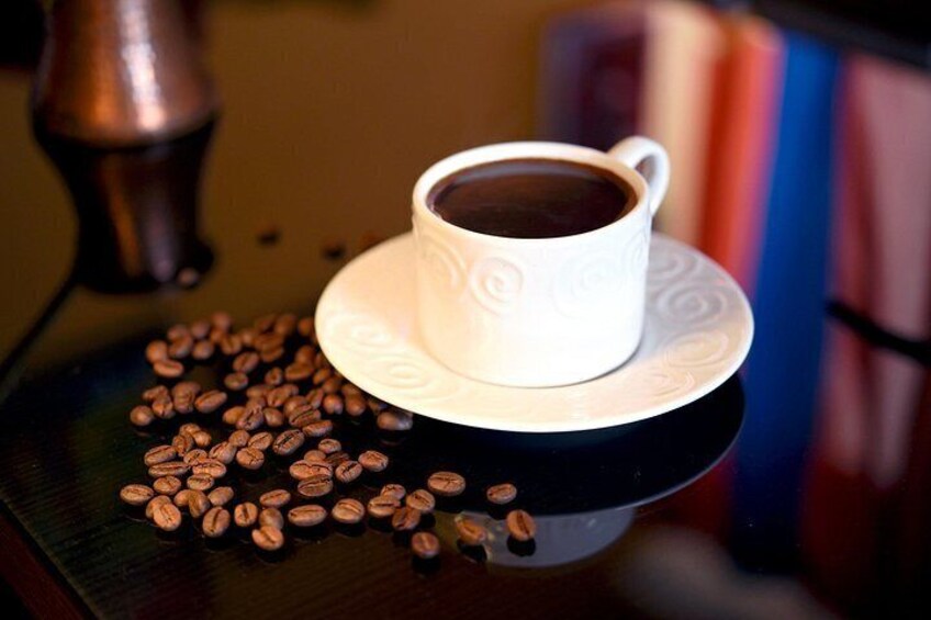 A cup of coffee on a saucer with coffee beans scattered around. 3