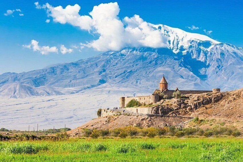A snow-capped mountain, a historic building, and a green field. 2