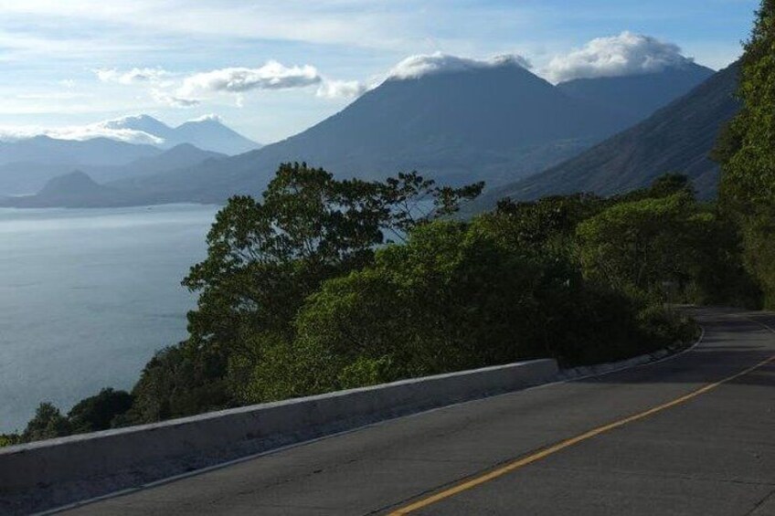 A winding mountain road with a view of a large body of water and distant mountains. 4