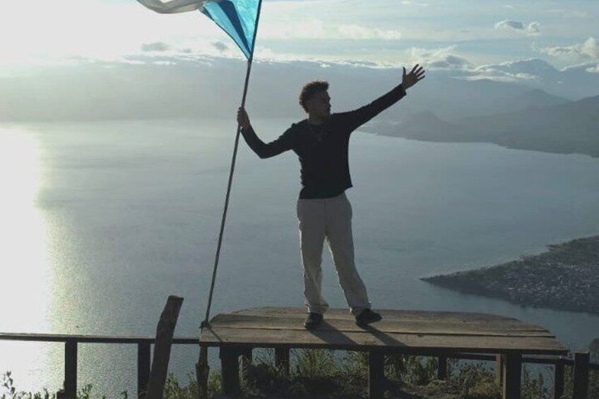 A person standing on a wooden platform overlooking a body of water with mountains in the distance. 5