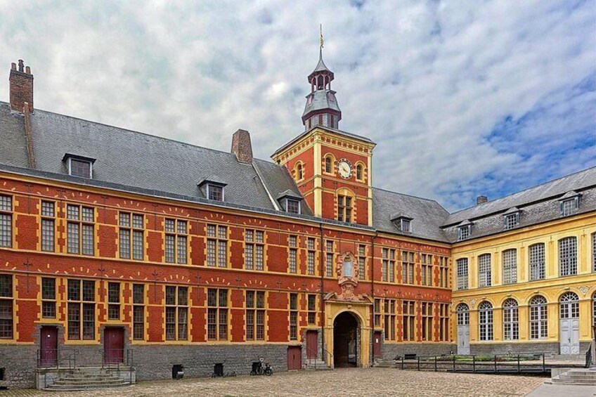En historisk bygning med et tårn, der bærer et ur, en facade af røde mursten og buede vinduer. 2