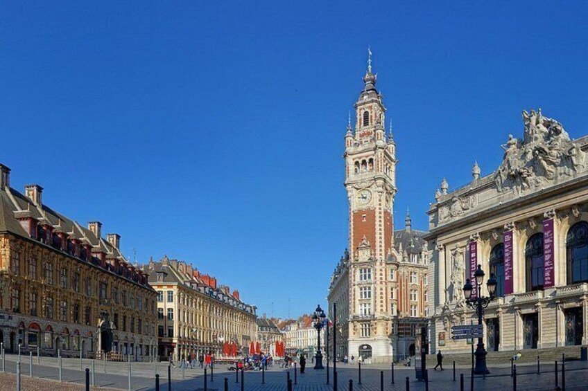 Ett historiskt torg med ett imponerande klocktorn, vackert utsmyckade byggnader och en klarblå himmel. 3