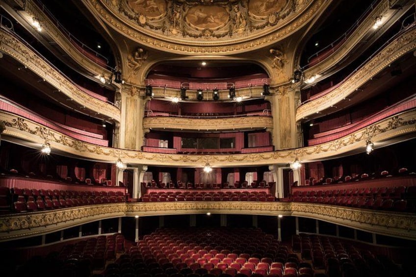 Een versierde theaterzaal met rode zitplaatsen en een groot, rond podium. 2