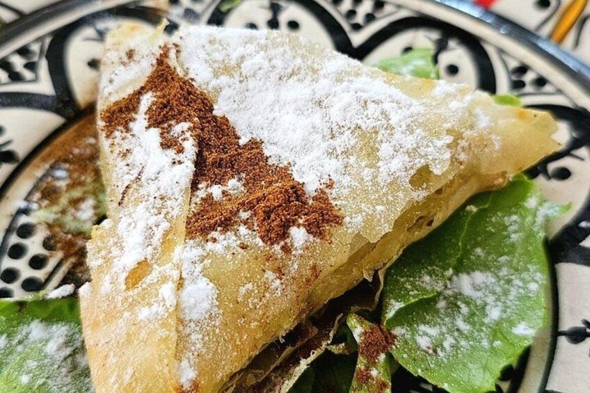 A pastry with powdered sugar and cinnamon on a patterned plate. 3