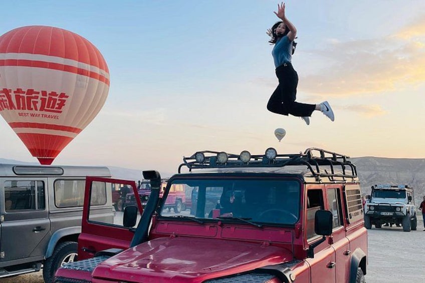 Eine Person springt von einem Fahrzeug mit einer Heißluftballon im Hintergrund. 1
