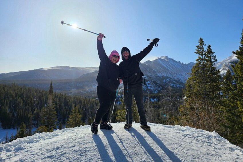 Två personer åker skidor på ett snötäckt berg med klar himmel och en sjö i bakgrunden. 3