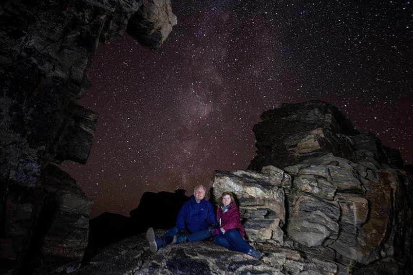 Two people sitting on a rock formation under a starry night sky. 4