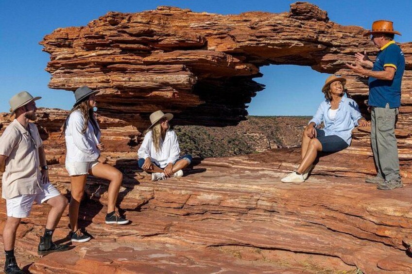 En grupp människor sitter och står på en klippavsats med en stor klippformation i bakgrunden. 1