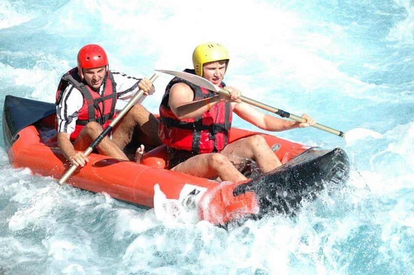 Two people in a red inflatable raft on a river with white water rapids. 3