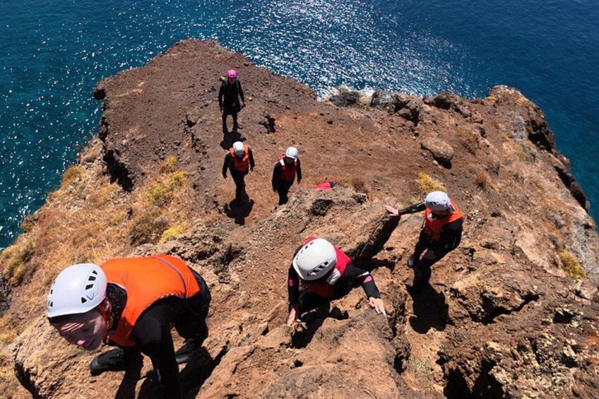 A group of people climbing a rocky cliff by the sea. 5