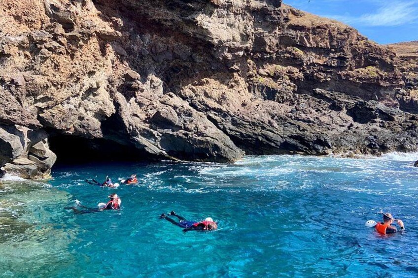 People swimming in a clear blue sea with rocky cliffs in the background. 2