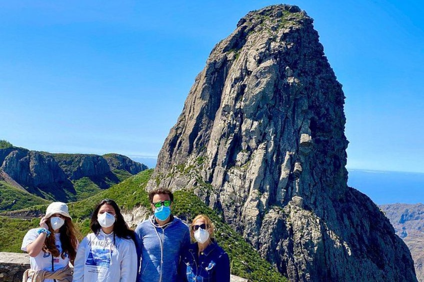 A group of people standing in front of a tall, rocky mountain peak with a clear sky in the background. 2