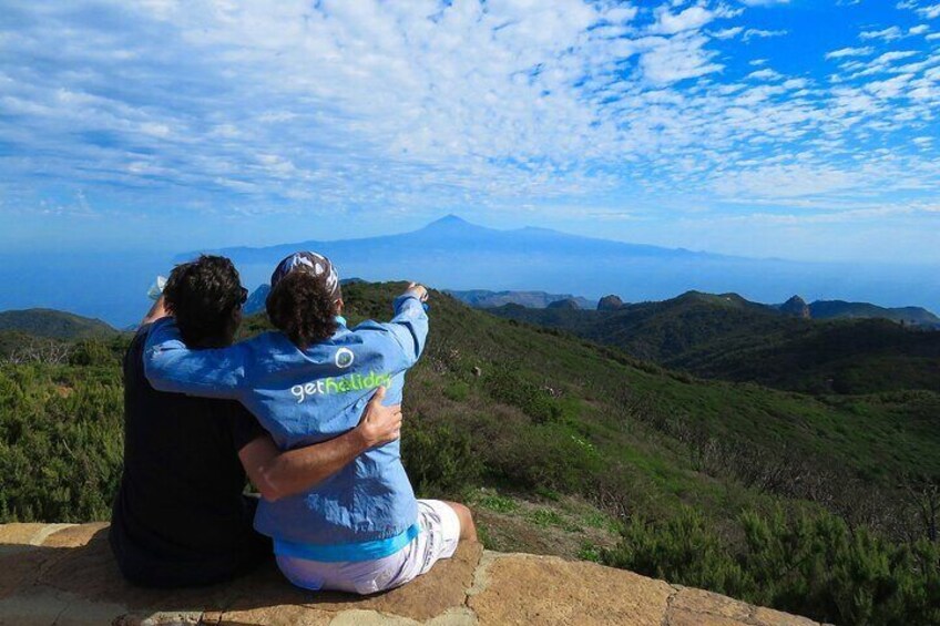 Two people sitting on a ledge overlooking a mountainous landscape. 3
