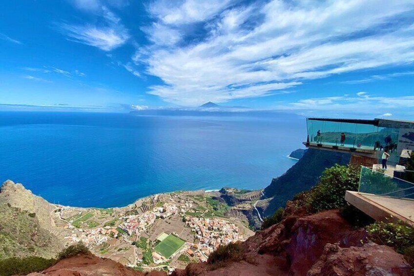 A coastal landscape with a glass bridge overlooking the sea, a rocky terrain, and a distant view of a town. 4