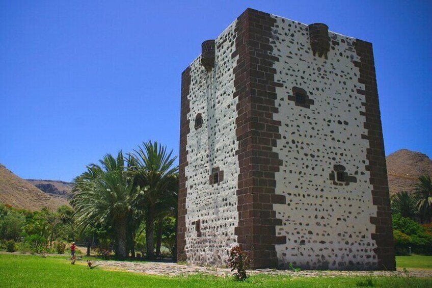 A tall, square tower with a patterned facade, surrounded by greenery and palm trees, with mountains in the background. 5