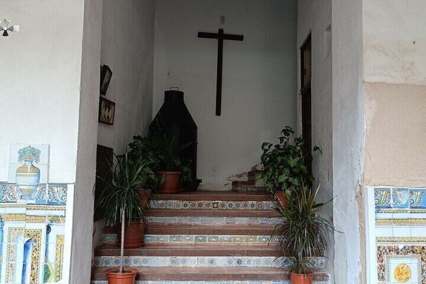 Una escalera adornada con plantas en macetas, una cruz en la pared y baldosas con diseño. 1