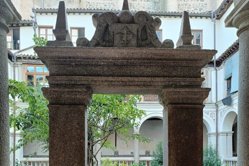 A stone archway with intricate carvings, surrounded by buildings and greenery. 1