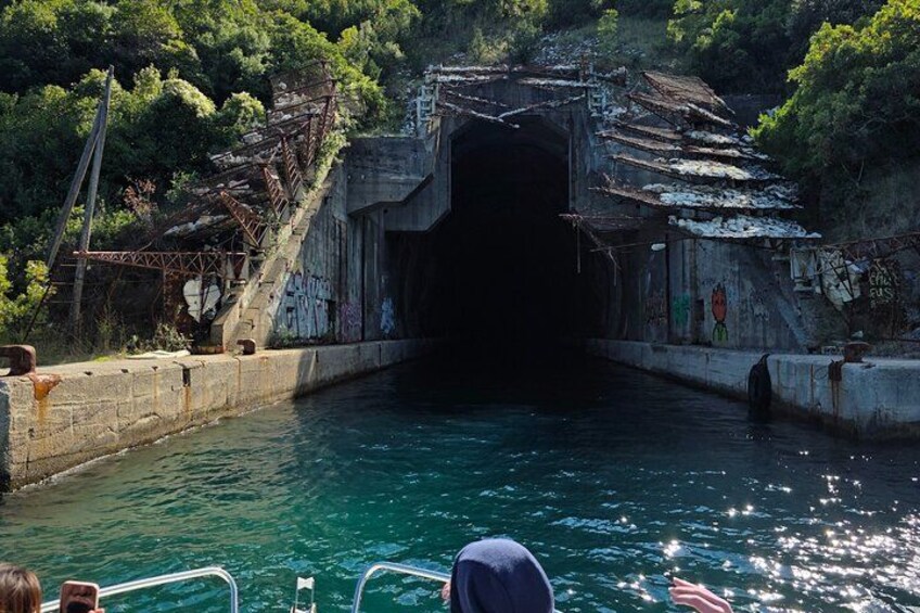 Un bote navegando por una vía fluvial estrecha con la entrada a un túnel, rodeado de vegetación y una estructura deteriorada. 4