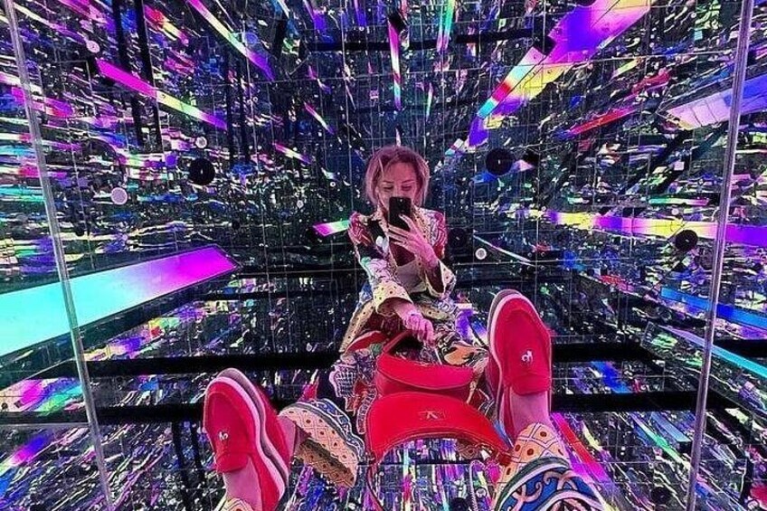 A person sitting on a chair in a room with a mirrored ceiling and walls, surrounded by colorful lights. 2