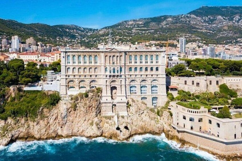 A coastal cityscape with a prominent historical building, rocky cliffs, and a clear blue sea. 2