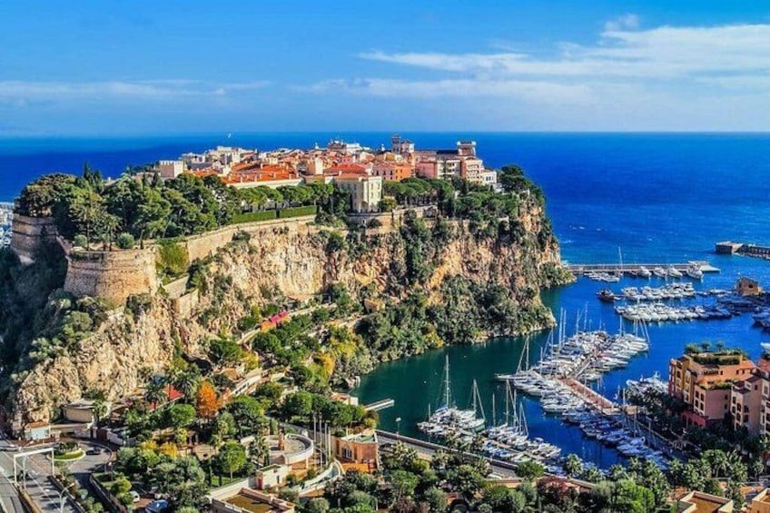 A coastal town with a historic fortification, a marina with boats, and a cliff overlooking the sea. 1