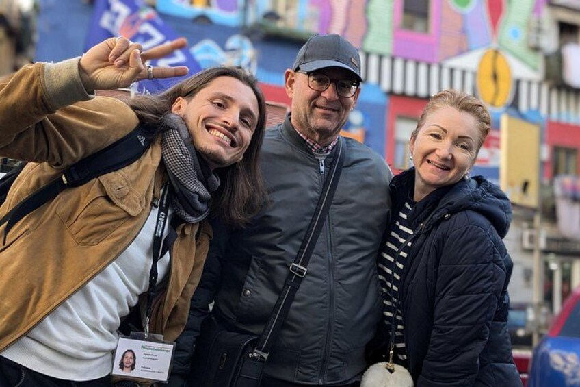 Tres personas posando para una foto en un entorno urbano con edificios coloridos al fondo. 3