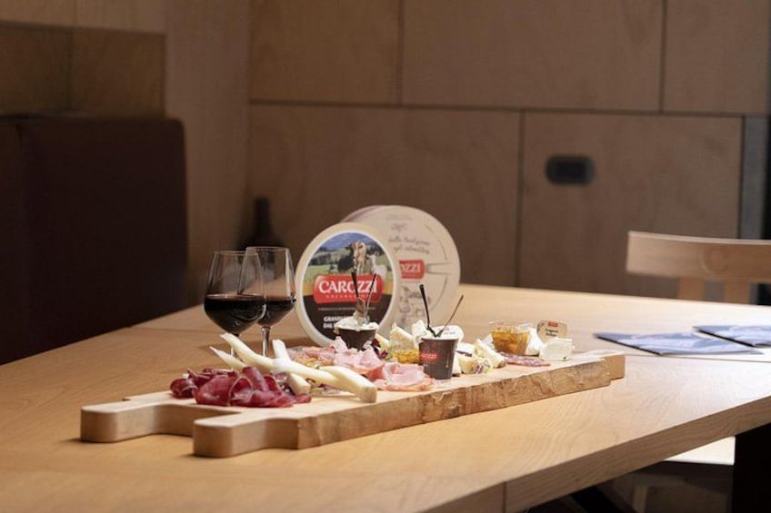 A wooden table with a food platter, two glasses of red wine, and a pizza box. 2