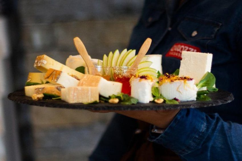 A person holding a tray with various cheeses, fruits, and nuts. 4