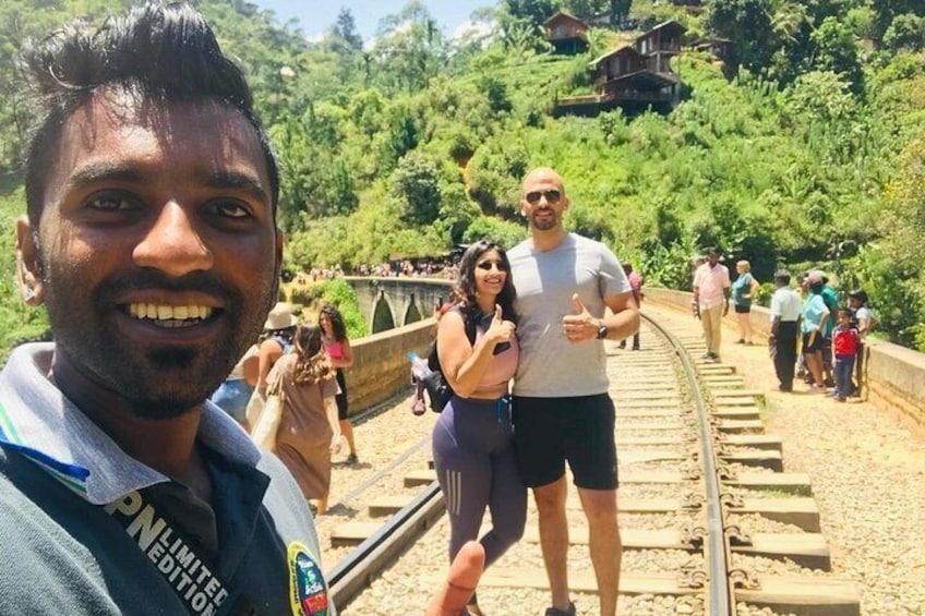 A railway track with people walking on it, surrounded by greenery and a bridge in the background. 3