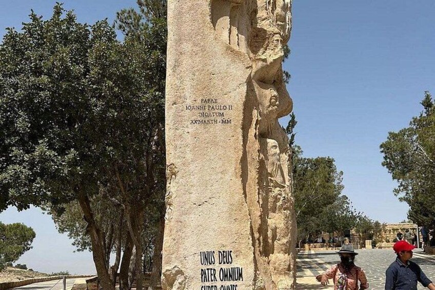 A stone monument with inscriptions, surrounded by trees and a clear sky. 2