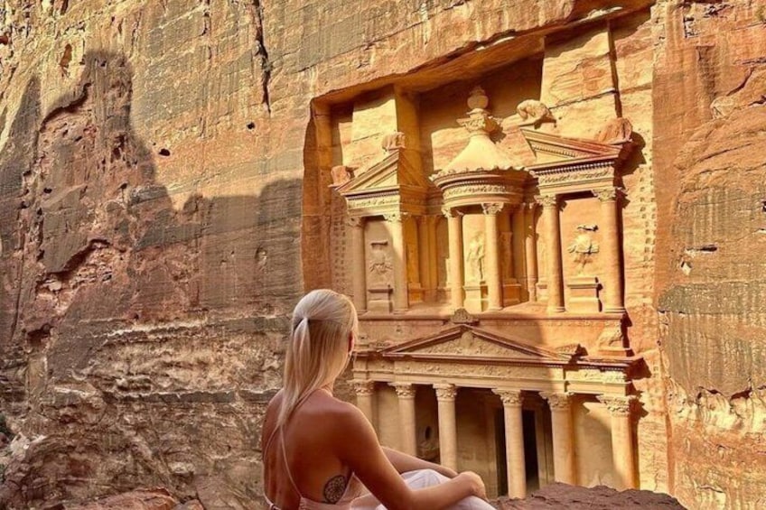 A person sitting in front of a rock-carved structure with columns and a pediment. 3