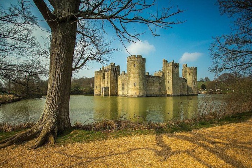 A castle by a calm lake with a large tree in the foreground. 1