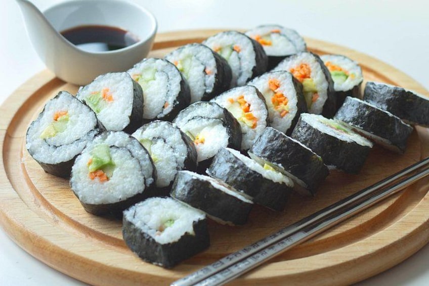A wooden plate with sushi rolls, a small bowl of soy sauce, and chopsticks. 2