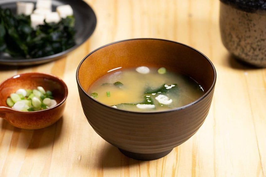 A bowl of clear soup with green onions, a small bowl of chopped green onions, and a plate of tofu and seaweed. 3