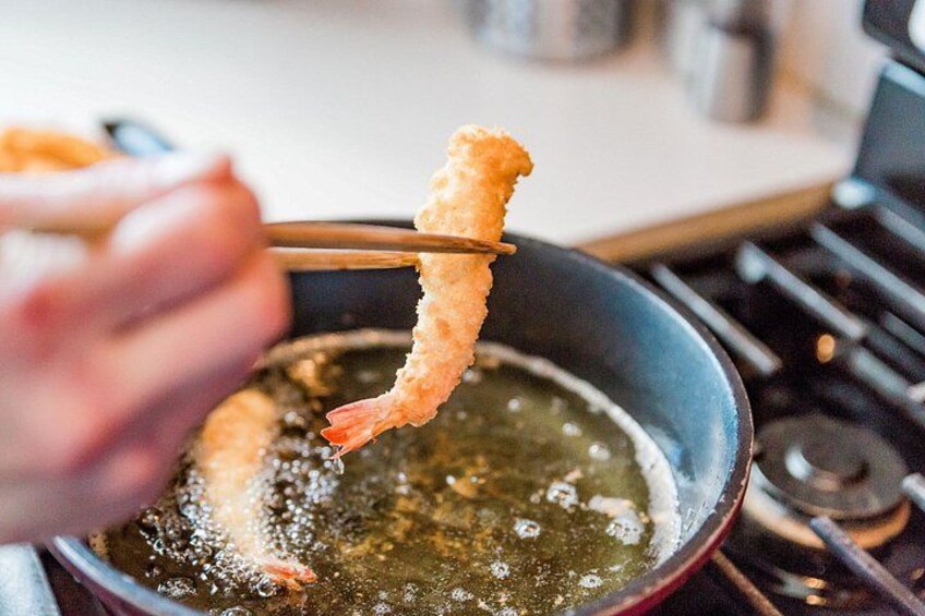 A hand holding a pair of chopsticks with a piece of fried food over a pan of oil. 3