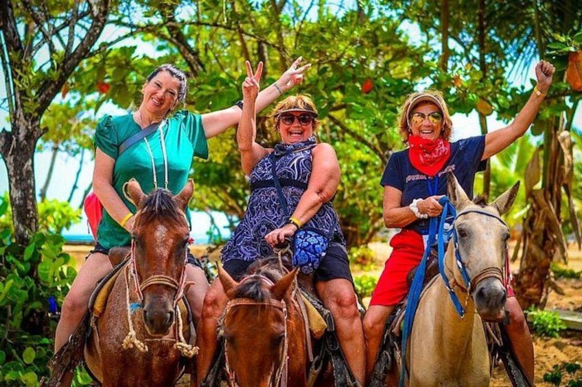Three people riding horses in a tropical setting with trees and greenery in the background. 2