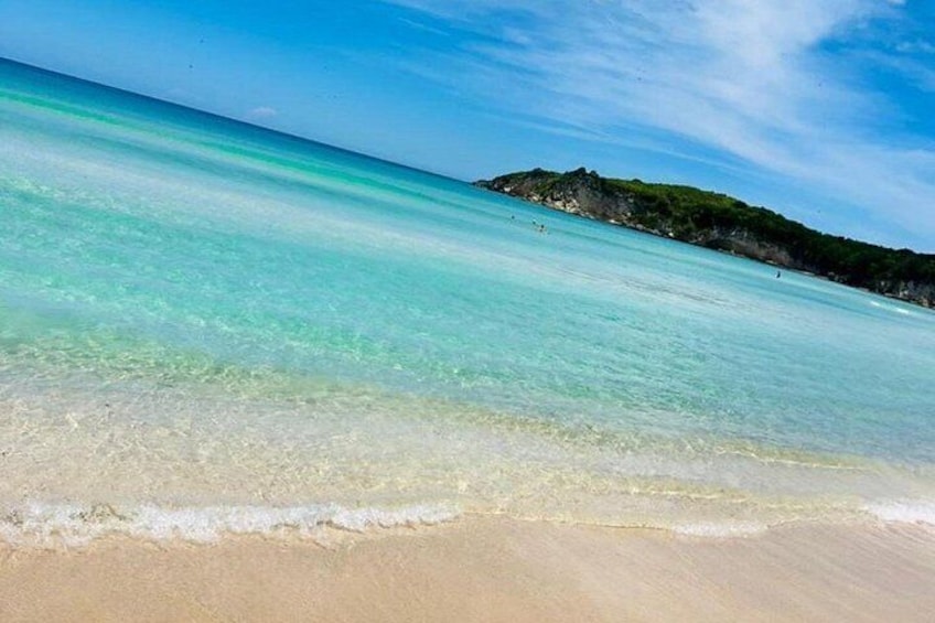 A beach with clear turquoise water, sandy shore, and a distant rocky hill. 3